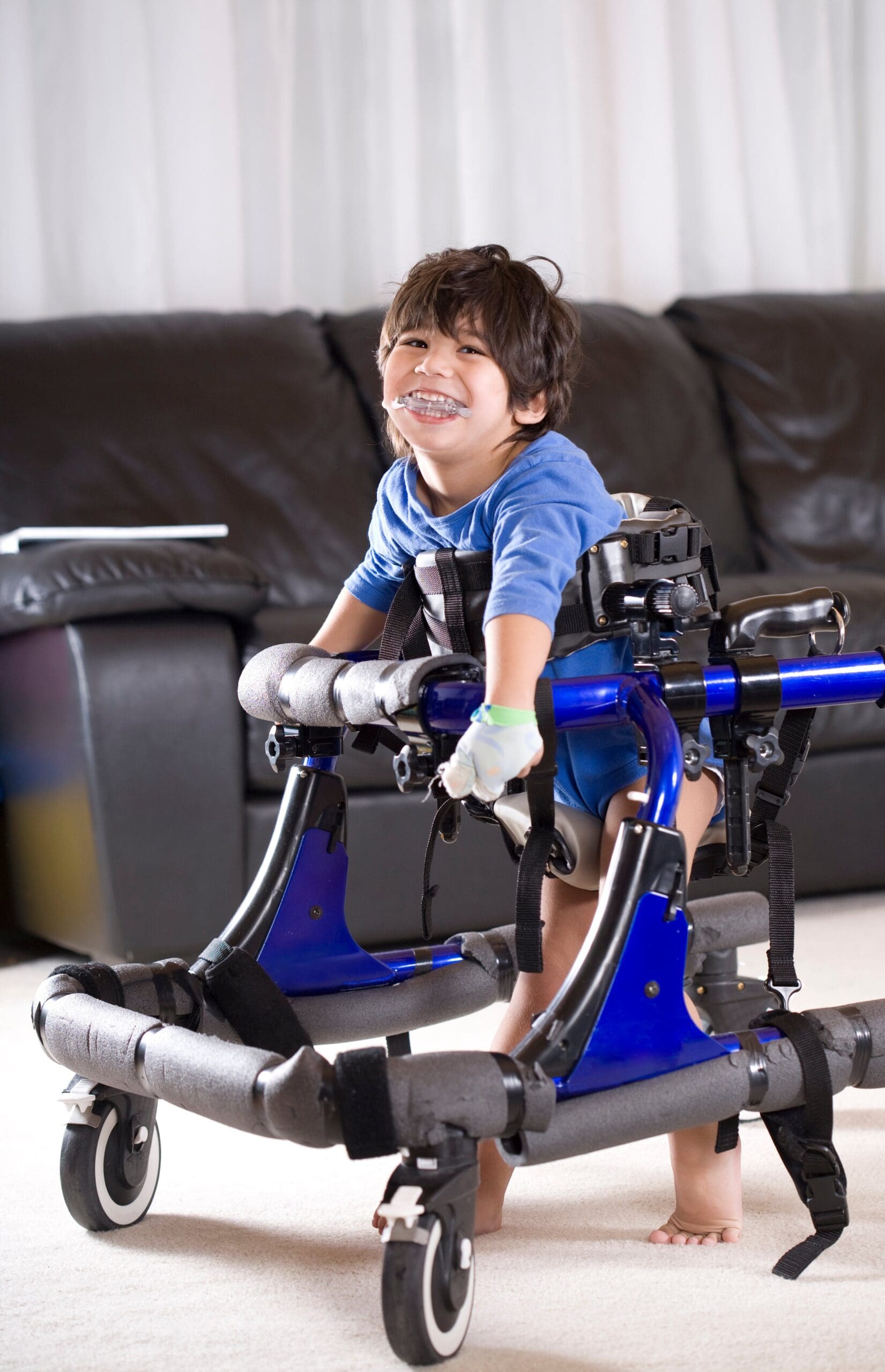 Young boy with cerebral palsy using a gait trainer and smiling.